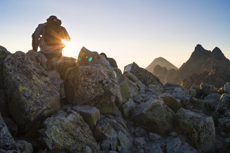 Free Image of Climber resting on rocky mountain peak at sunrise 