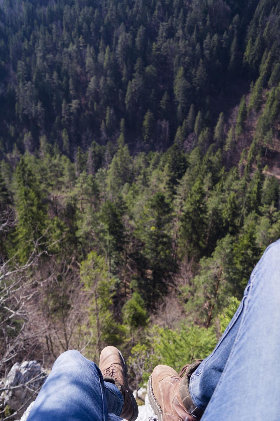 Free Image of Person’s legs dangling from cliff with forest below 