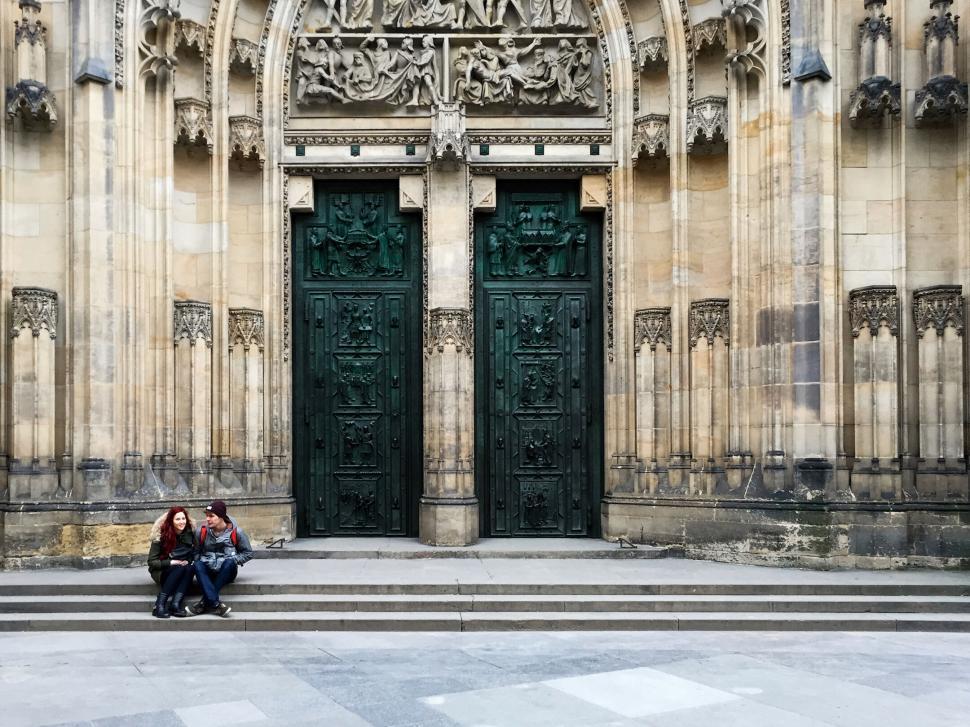 Free Image of Two people seated on steps before grand historic portal. 