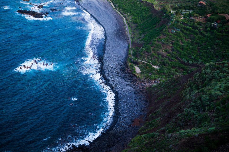 Free Image of Rocky coastline with green hills and blue ocean waves. 