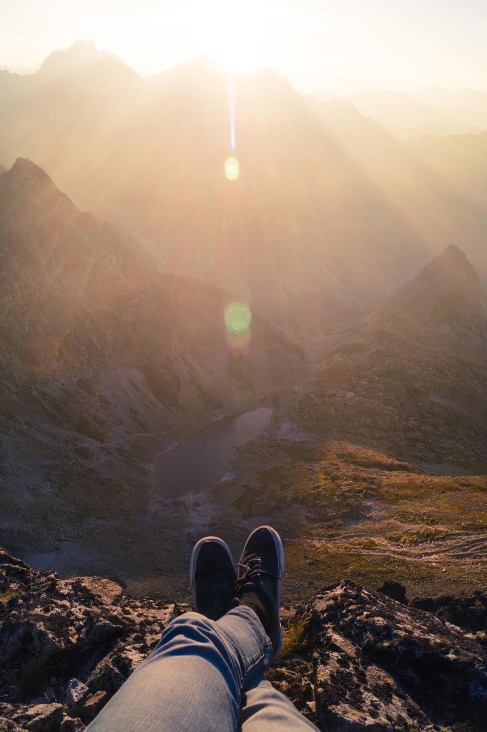 Free Image of Person s feet dangling over mountain valley at sunrise. 