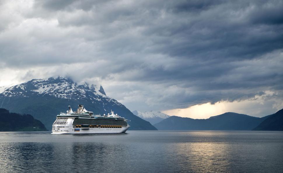 Free Image of Cruise ship sailing on a calm water surrounded by mountains. 