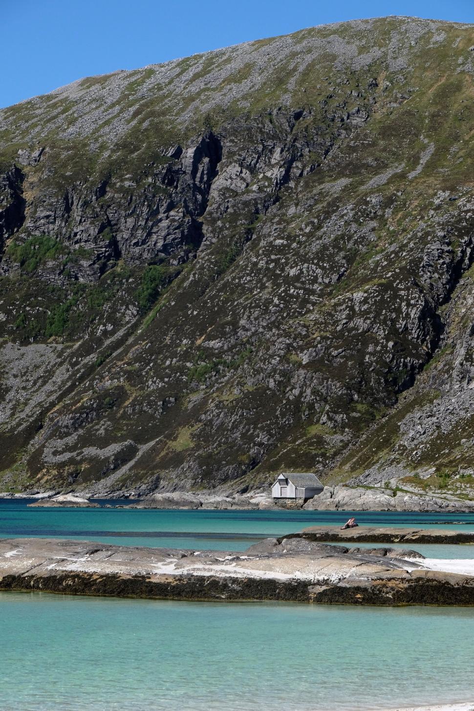 Free Image of Small house near steep mountain and blue ocean water. 
