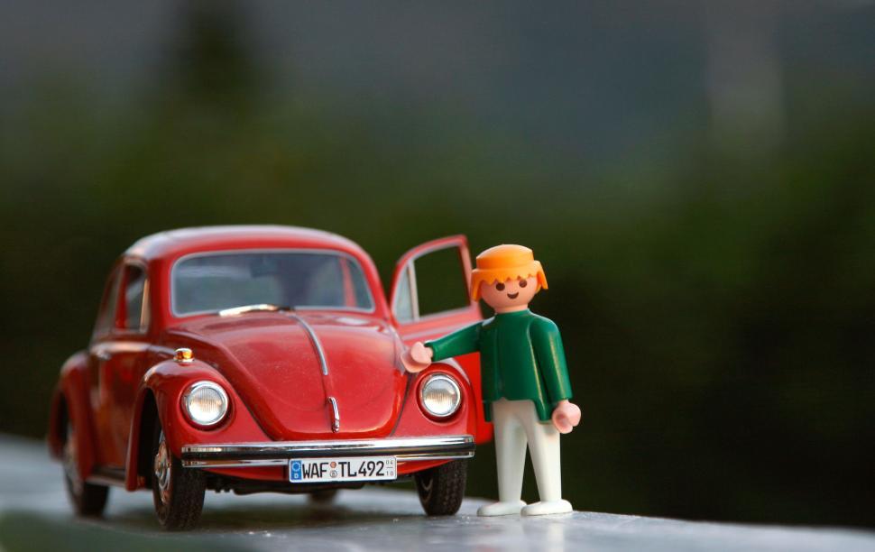 Free Image of Toy figure standing beside a vintage red toy car. 