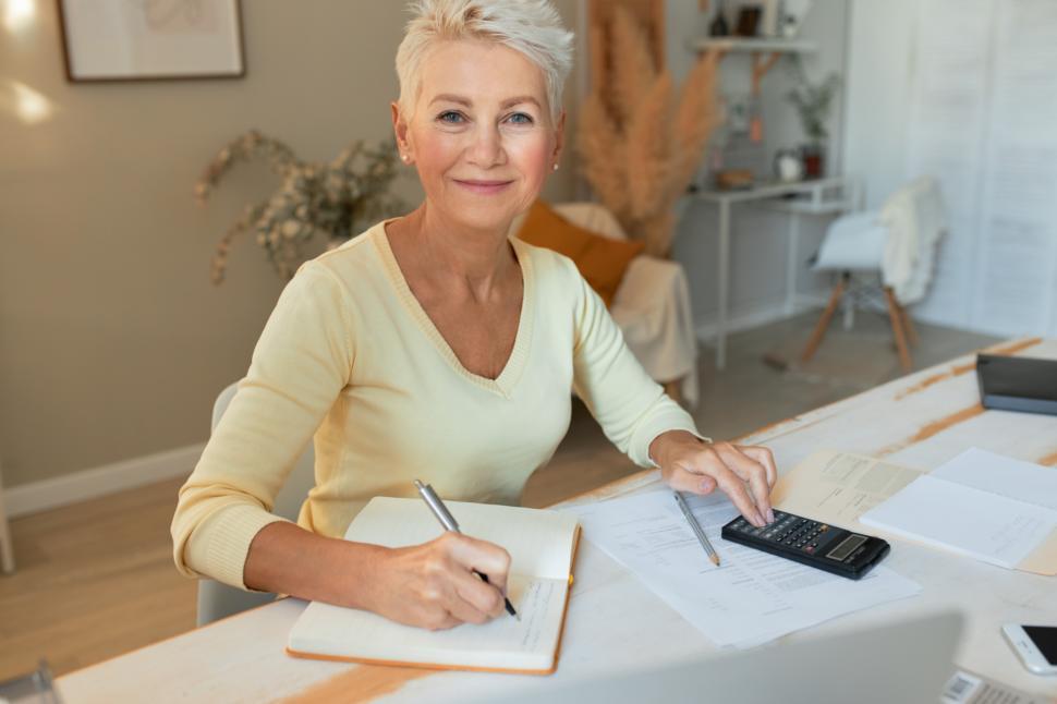 Free Image of Accounting, bookeeping and finances. Portrait of stylish mature female economist working from home, sitting at desk with documents and calculator, doing paperwork, analyzing budget, writing down 