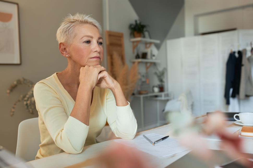 Free Image of Indoor shot of sad frustrated middle aged businesswoman sitting at office table with hands under chin having financial problems, thinking about new business strategy during economic crisis 