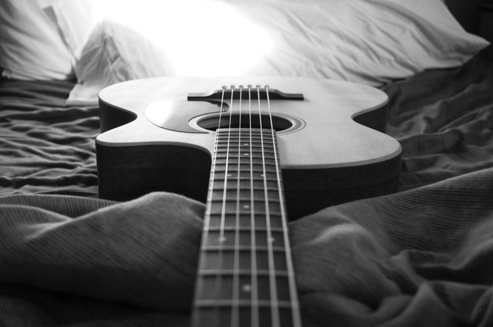 Free Image of Acoustic guitar lying on bed with soft lighting. 