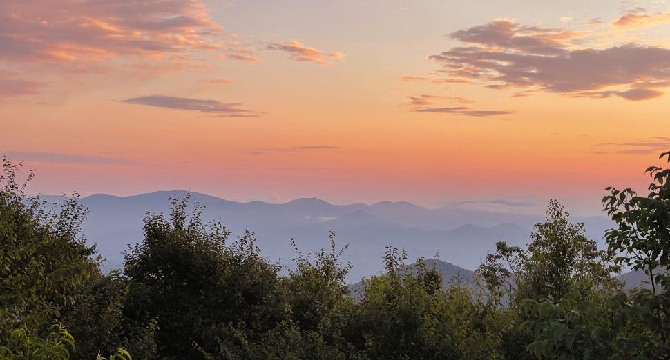 Free Image of A serene sunset over distant mountains with trees 