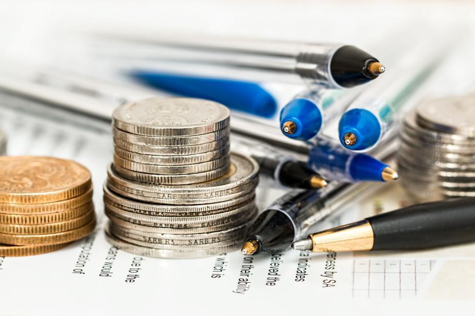 Free Image of Coins stacked with pens on documents in office setting 