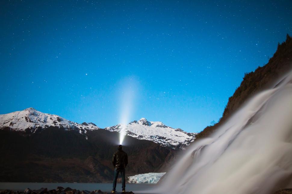 Free Image of Man with flashlight under starry sky near snowy mountains. 