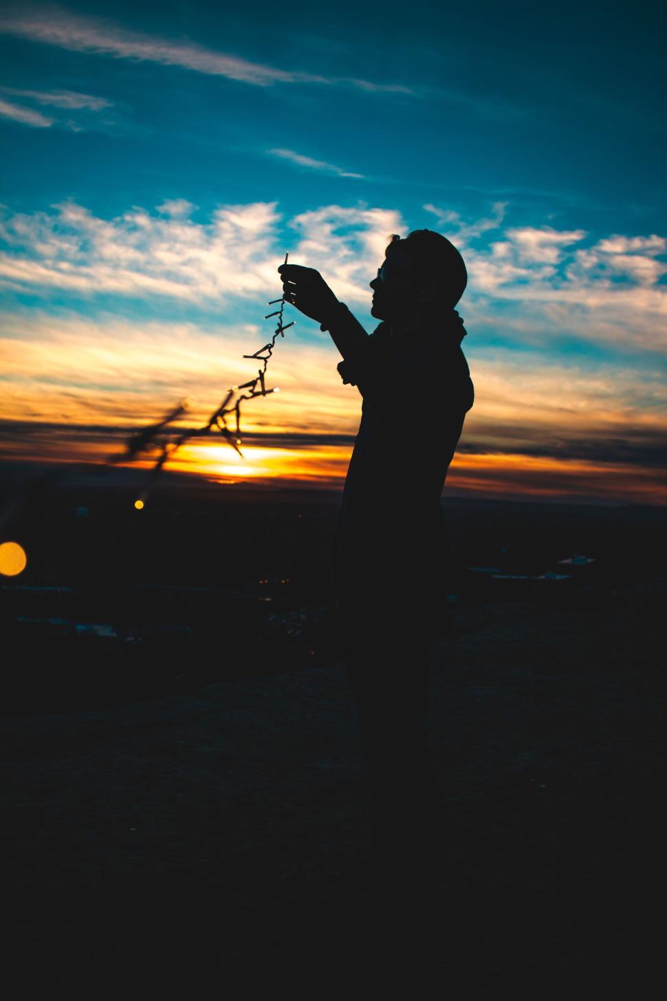 Free Image of Silhouette of person holding string lights at sunset. 