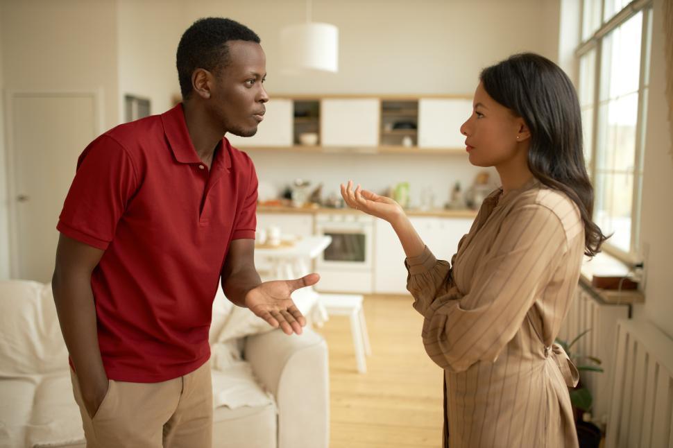 Free Image of Man and woman of black ethnicity arguing in living-room, gesticulating, proving each of them right, handsome male in red explaining reason of his behavior, attractive elegant woman crossing her arms 