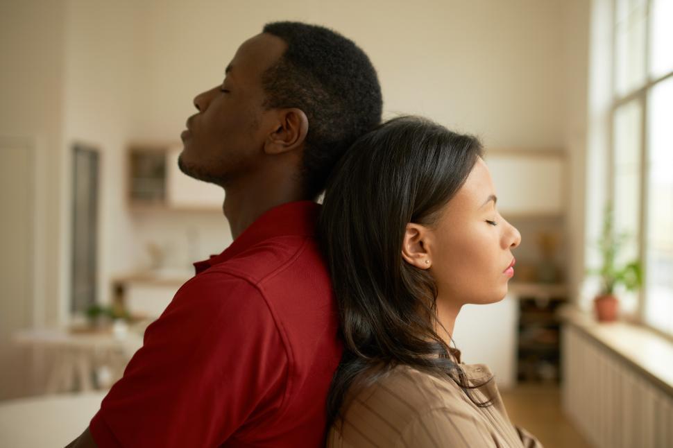 Free Image of Picture of black man and woman standing back to back with eyes closed, feeling exhausted and offended after sorting things out isolated on blurred background of living-room. Human relationships 