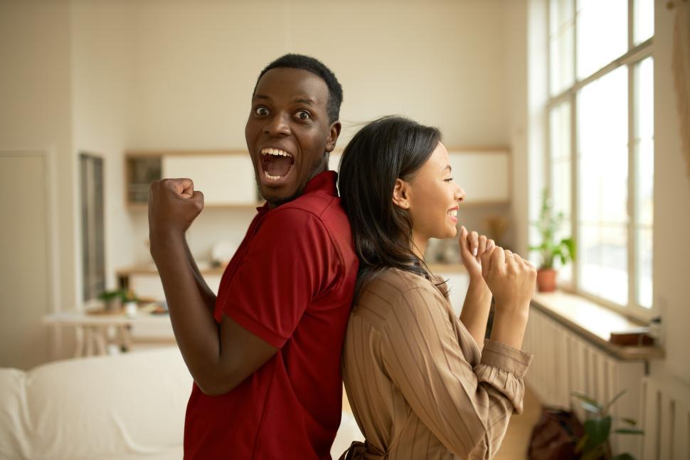 Free Image of Happy cheerful African American female and male standing back to back in lounge clenching fists with triumph, screaming with joy celebrating successful beginning of their business or winning money 