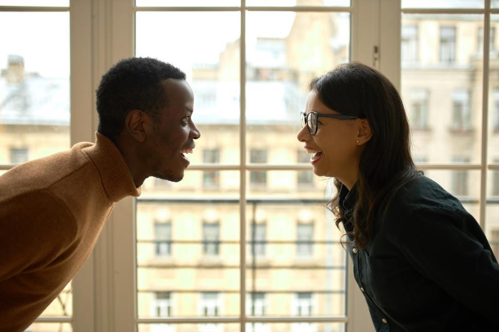 Free Image of Cropped picture of man and woman looking at each other with happy, surprised and cheerful face expressions against wide window, celebrating purchase of their own property, female wearing glasses 