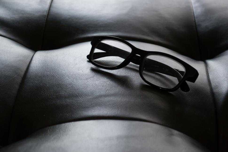 Free Image of Black framed glasses resting on black leather cushion 
