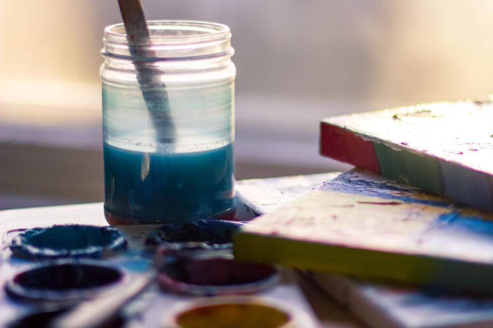 Free Image of Paintbrush in a jar of water amid art supplies scene. 