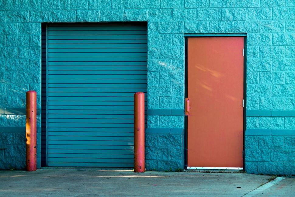 Free Image of Blue building wall with orange door and red pillars. 