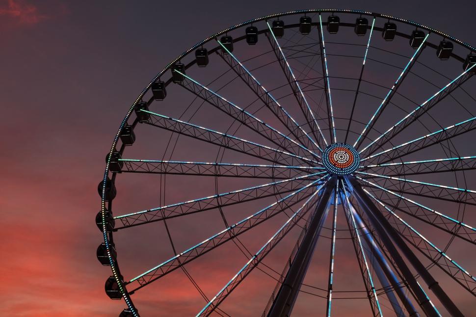 Free Image of Ferris wheel against a sunset sky with lights on spokes 