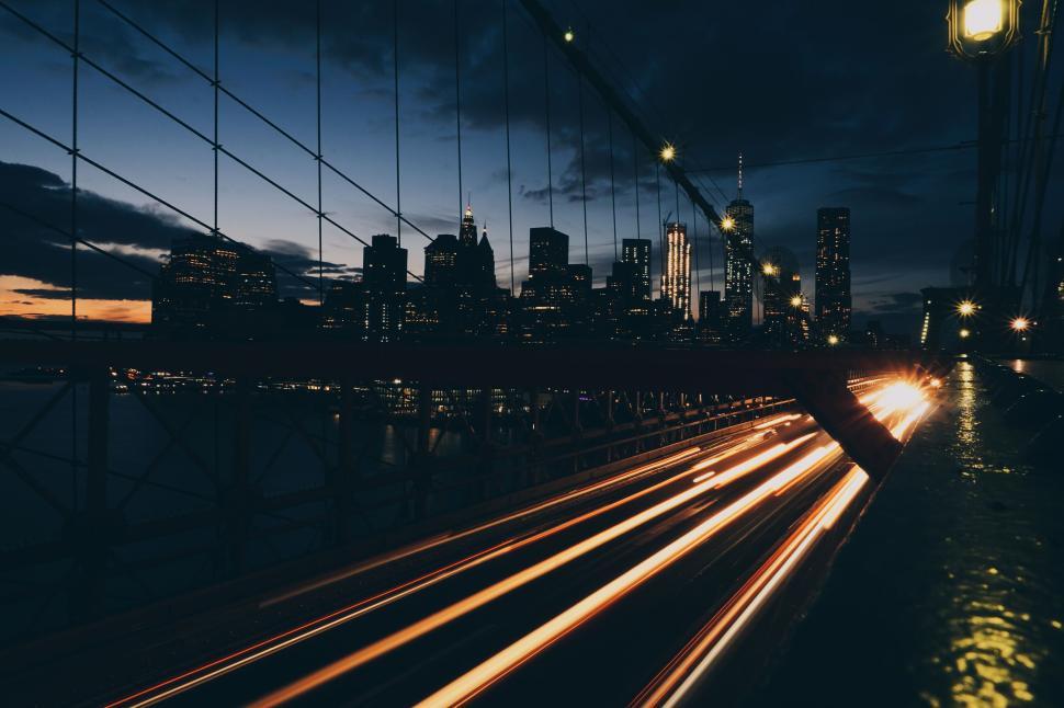 Free Image of Speeding light trails on bridge with city skyline 