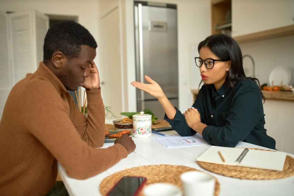 Free Image of Two young business partners male and female of black ethnicity sitting at kitchen table, discussing clue moment of delivery goods agreement, pretty woman gesticulating, man touching head, thinking 