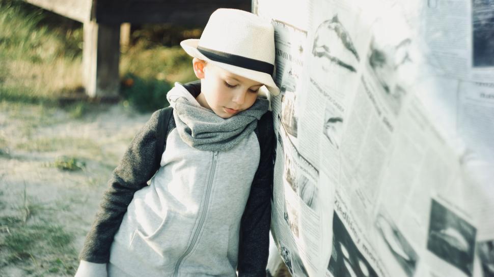 Free Image of Child wearing a hat and scarf leaning on newspapers 