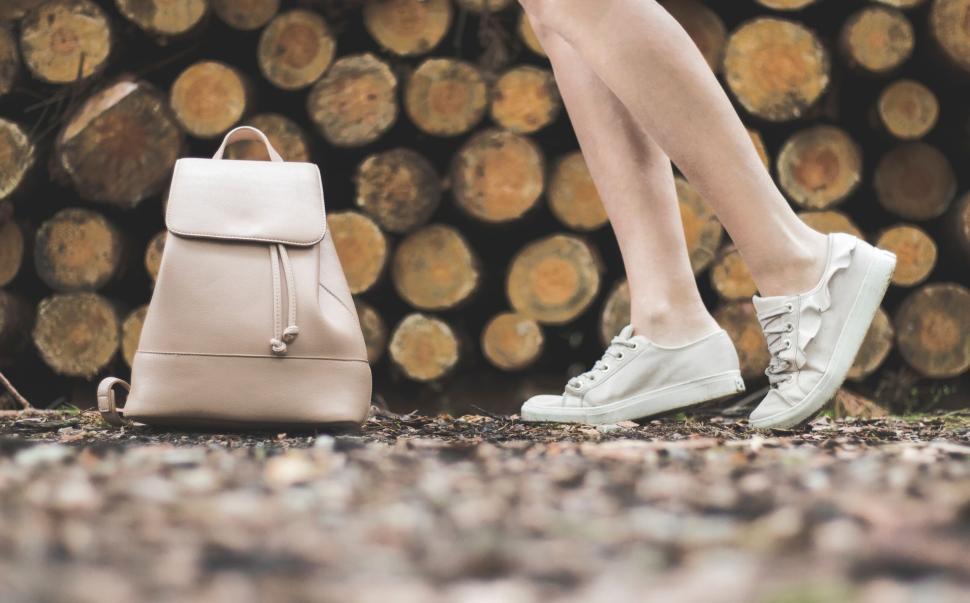 Free Image of Person with pink backpack walking near stacked logs. 