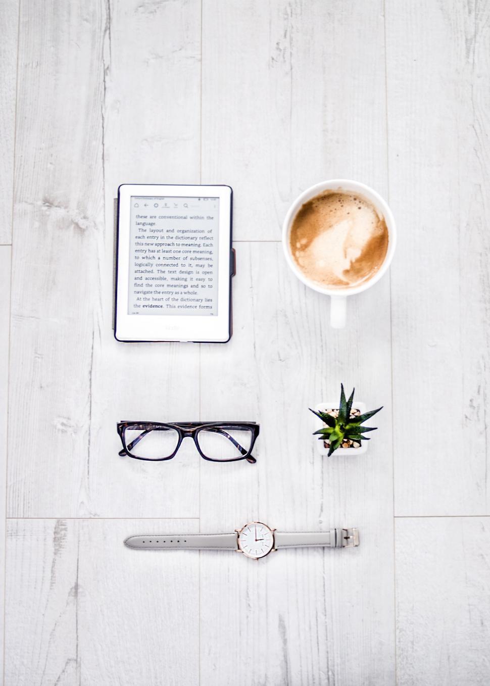 Free Image of Tabletop with e-reader, coffee, glasses, watch, plant. 