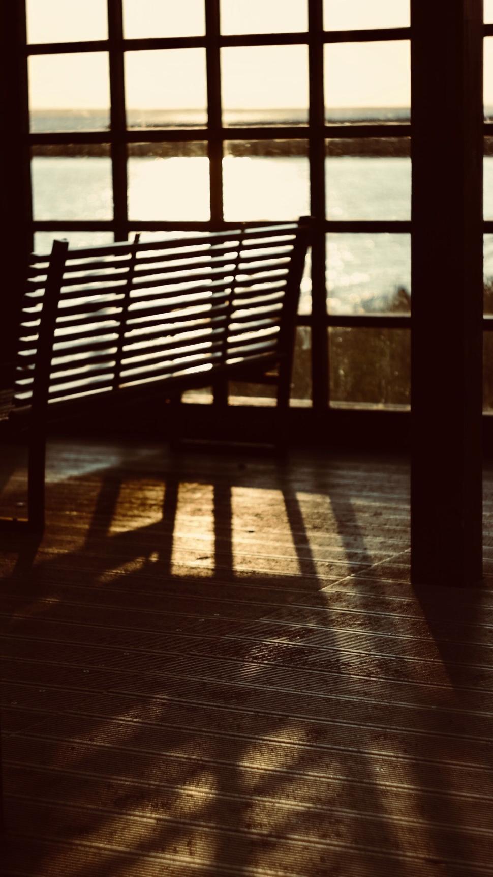 Free Image of Empty wooden bench casting shadows in a sunlit room. 
