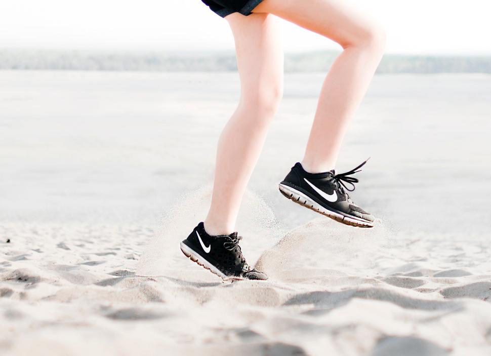 Free Image of Person jumping mid-air with Nike shoes on sandy beach. 