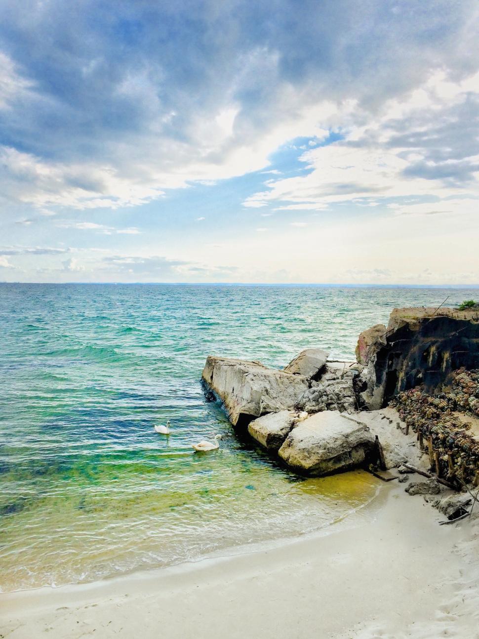 Free Image of Rocky coastline with blue green ocean and cloudy sky. 