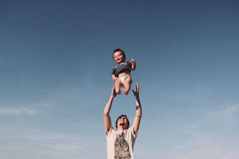 Free Image of Man lifting baby joyfully against clear blue sky 