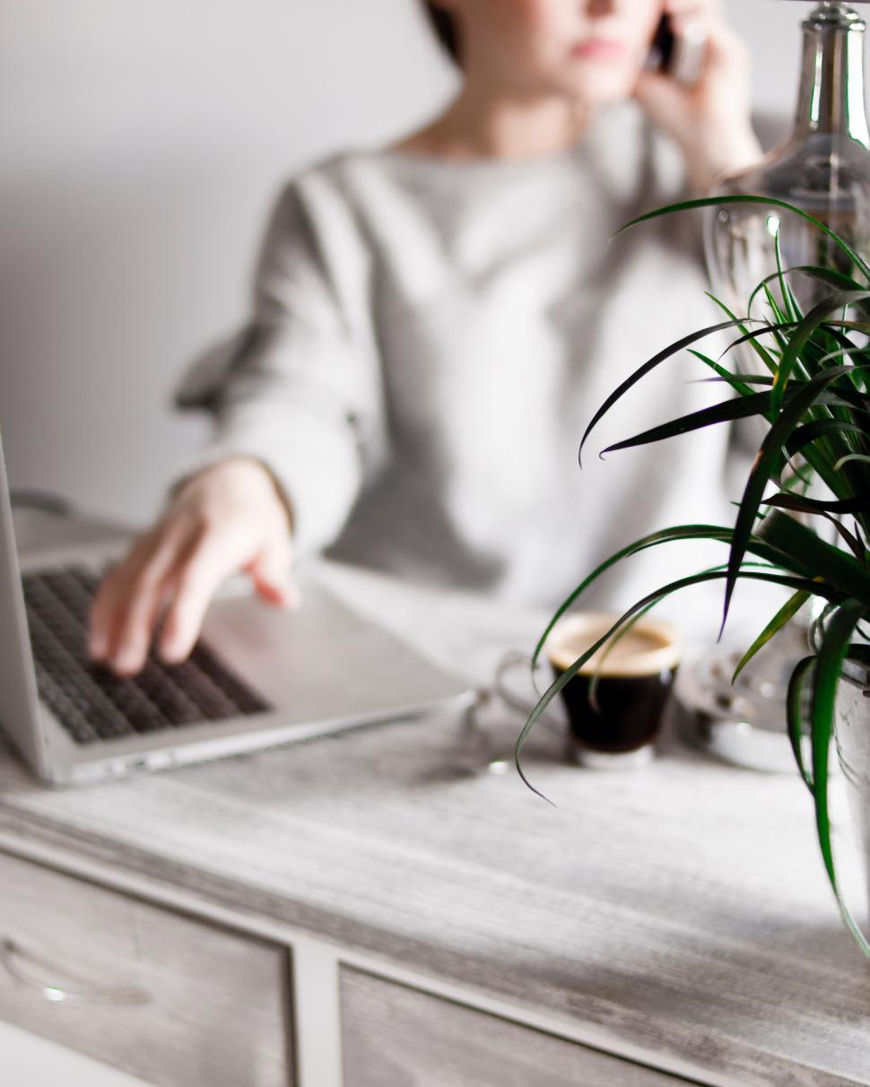 Free Image of Woman working on laptop while talking on phone. 