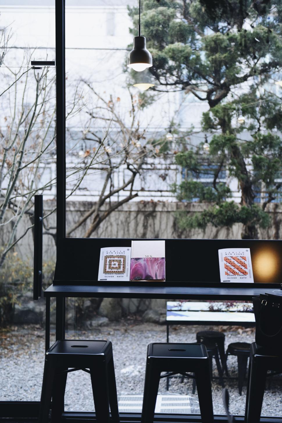 Free Image of Empty caf? table with books and stool near large window. 