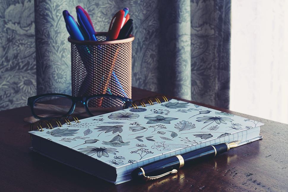 Free Image of Notebook and pen on a wooden desk with glasses and pens. 
