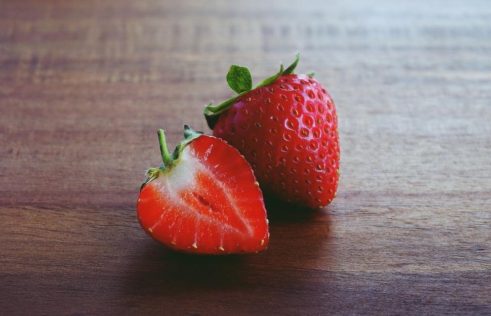 Free Image of Fresh strawberry on a wooden table, one cut in half. 