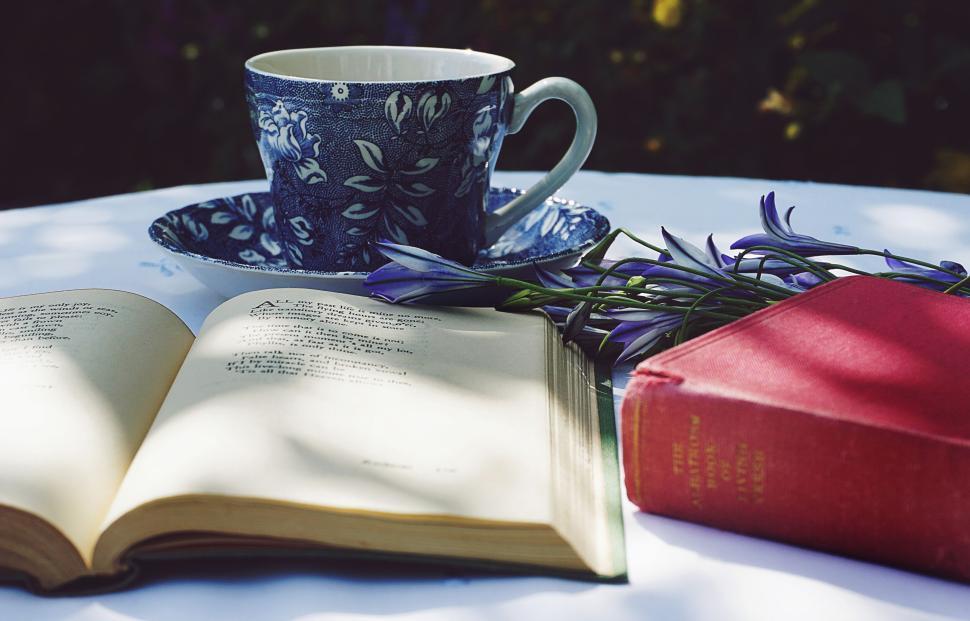 Free Image of Tea cup, open book, and flowers on a table outside. 