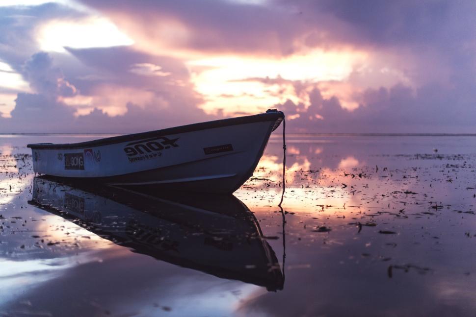 Free Image of Rowboat reflected in calm water during a serene sunset. 
