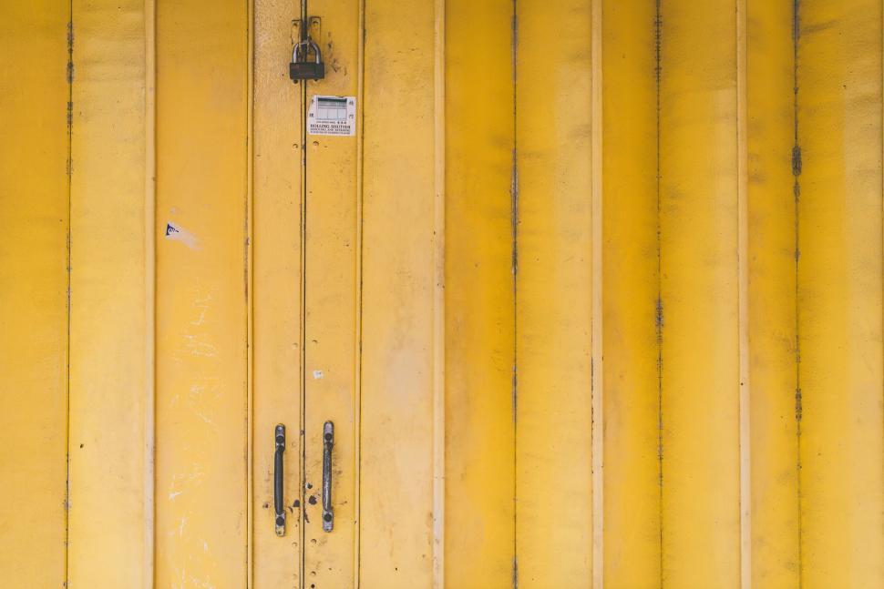 Free Image of Yellow metal door with a padlock and handles closed. 
