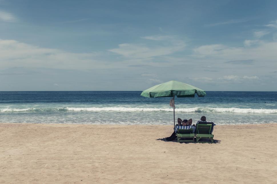 Free Image of Sunny beach with two people relaxing under umbrella 
