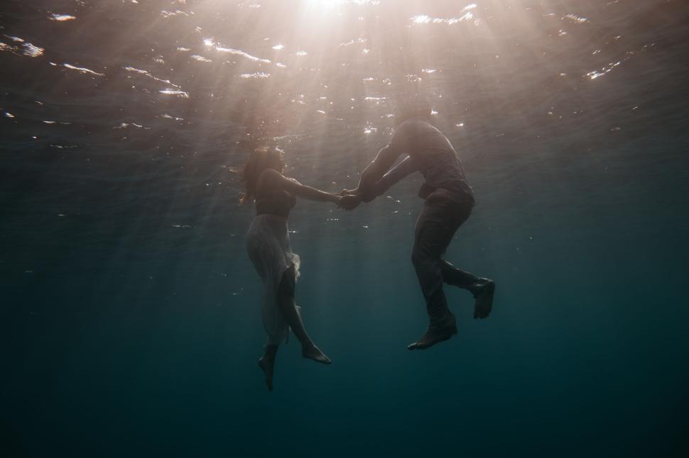 Free Image of Couple holding hands floating underwater gracefully. 