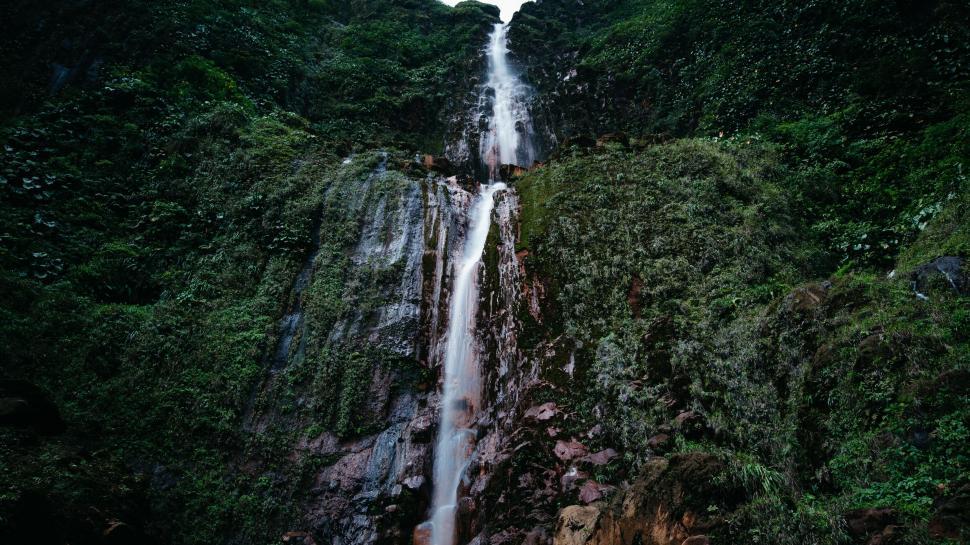 Free Image of Majestic waterfall cascading down lush green mountain 