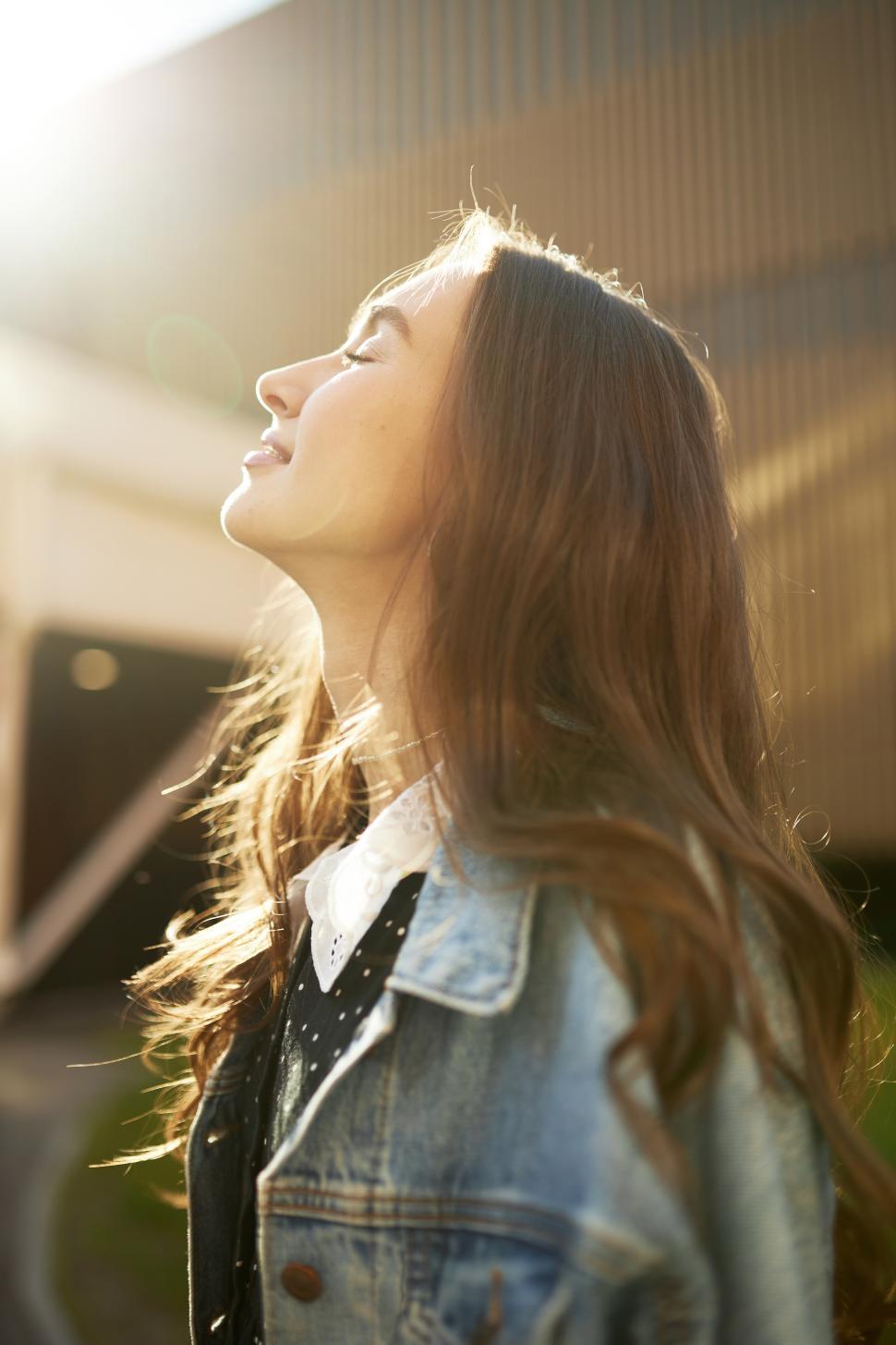 Free Image of Side view of beautiful charming caucasian girl of 20s with long hair in denim jacket enjoying warm spring day turning her face to sun with closed eyes during her summer stroll around city 