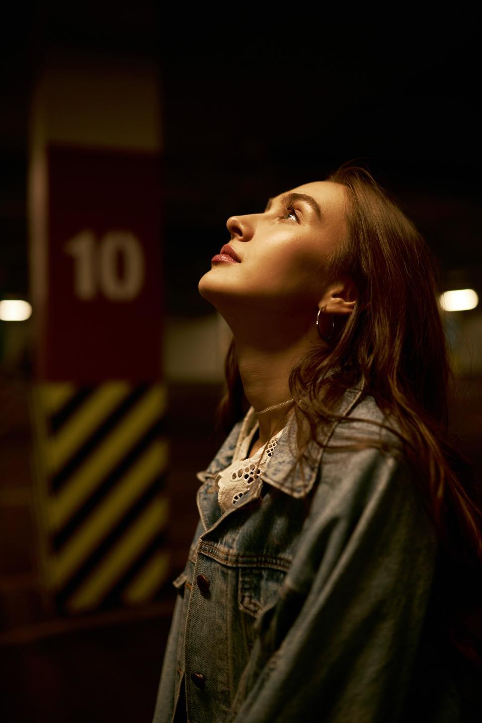 Free Image of Profile view of gorgeous dreamy romantic young lady in denim outfit looking up standing at empty parking lot, enjoying night walk alone, waiting for her friends to go to party together 