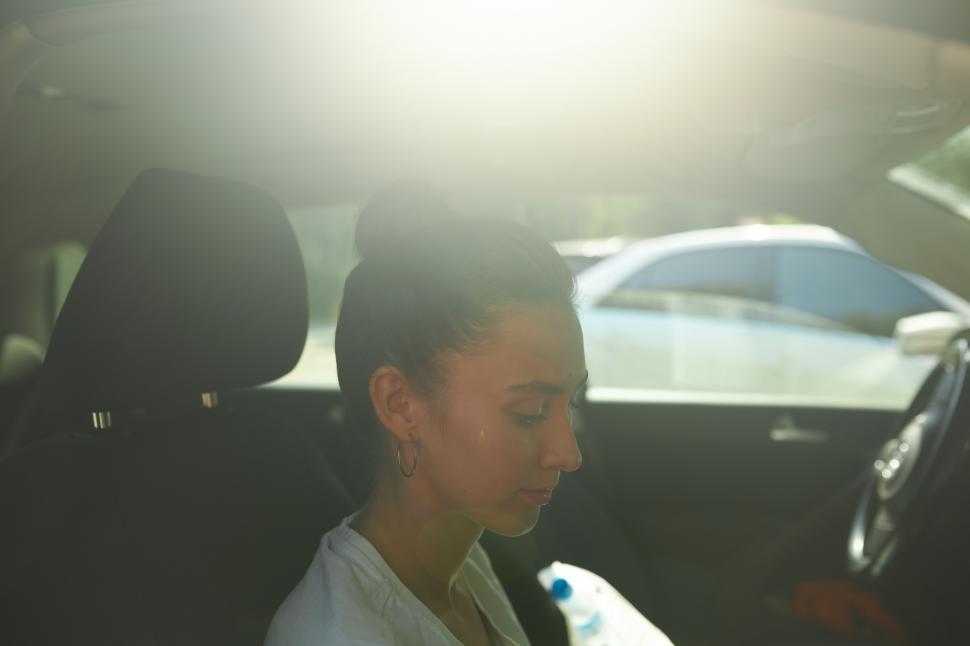 Free Image of Profile view of young female with hair bun in car sitting at passenger seat, looking down like using smartphone or reading book, waiting for driver to come back from shop or gas station 