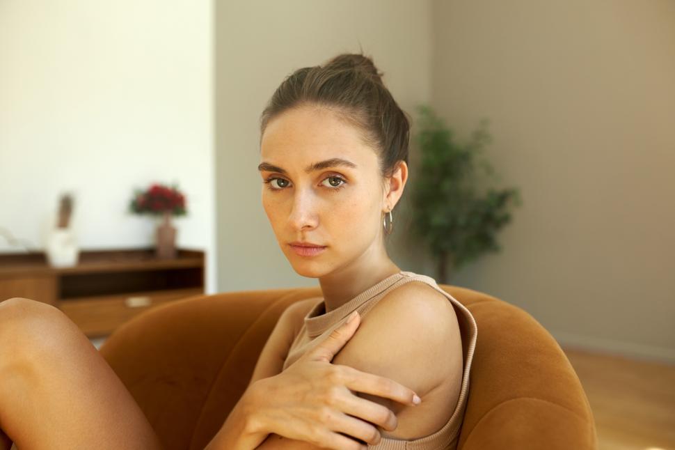Free Image of Attractive upset tired female looking at camera with pensive face sitting on sofa hugging herself giving self-protection after unpleasant conversation and breaking up with her boyfriend 