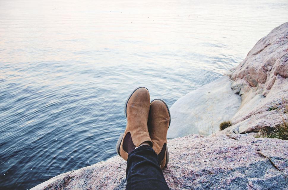 Free Image of Boots on rocky shore near calm body of water resting 