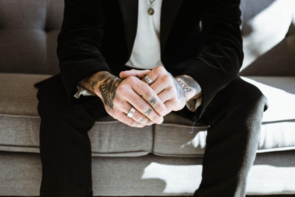 Free Image of Tattooed hands with rings resting on person s knees 