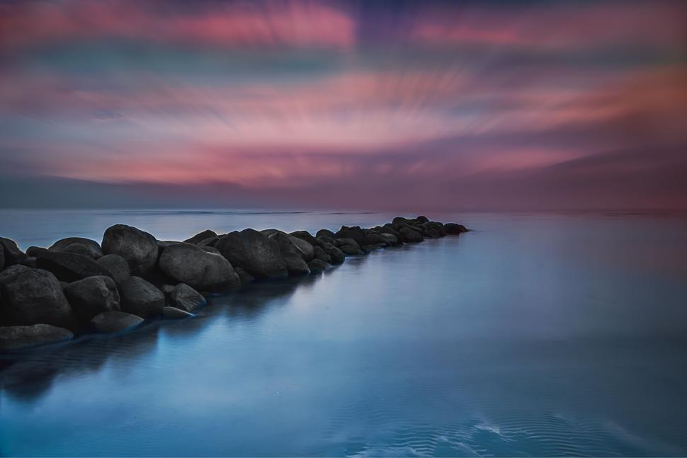 Free Image of Rocky pier extending into calm ocean during dusk 