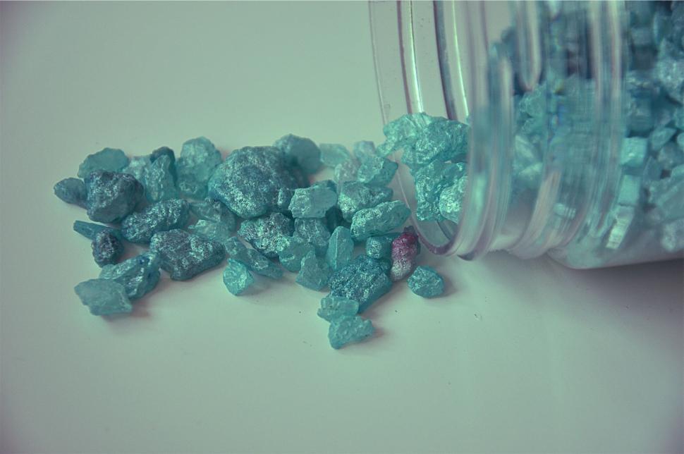 Free Image of Blue crystals spilled from glass jar onto white surface. 